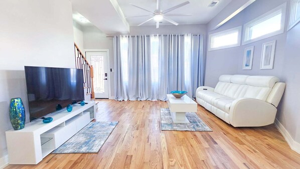 A modern living room with a flat-screen TV, white sofa, and a ceiling fan.
