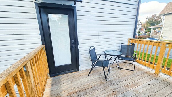 A wooden deck with a black door, a small table, and two chairs.
