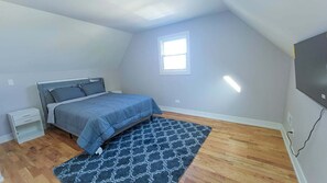 A bedroom with a bed, a nightstand, a window, and a TV.