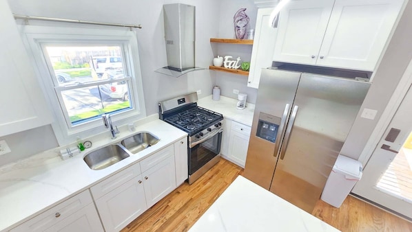 A compact kitchen with a gas stove, stainless steel appliances, a window, and a wooden floor. - Fabulous 3-bedroom townhome with AC in vibrant Chicago (Chicago)