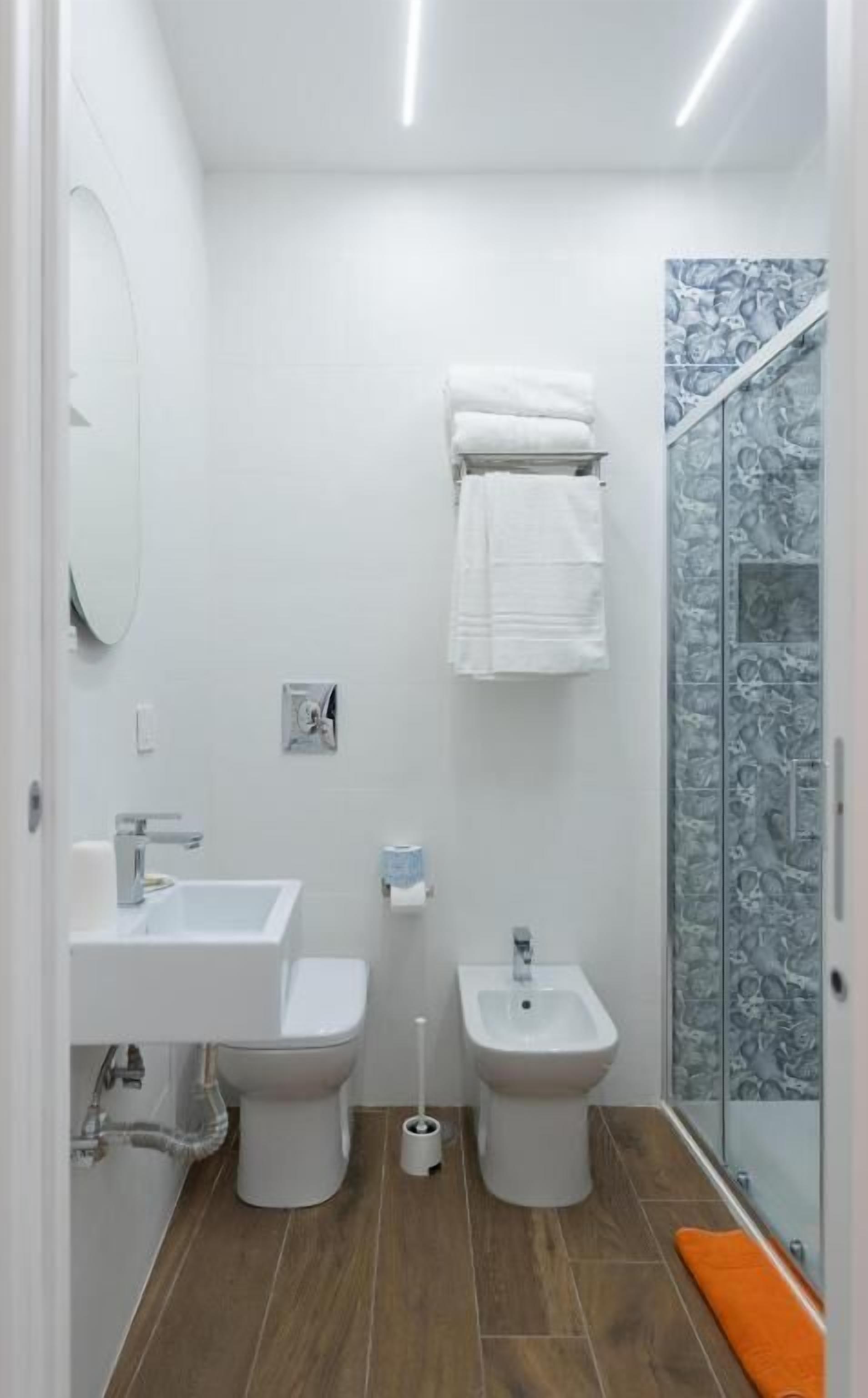 A bathroom with a toilet, bidet, sink, and shower with a marble wall.