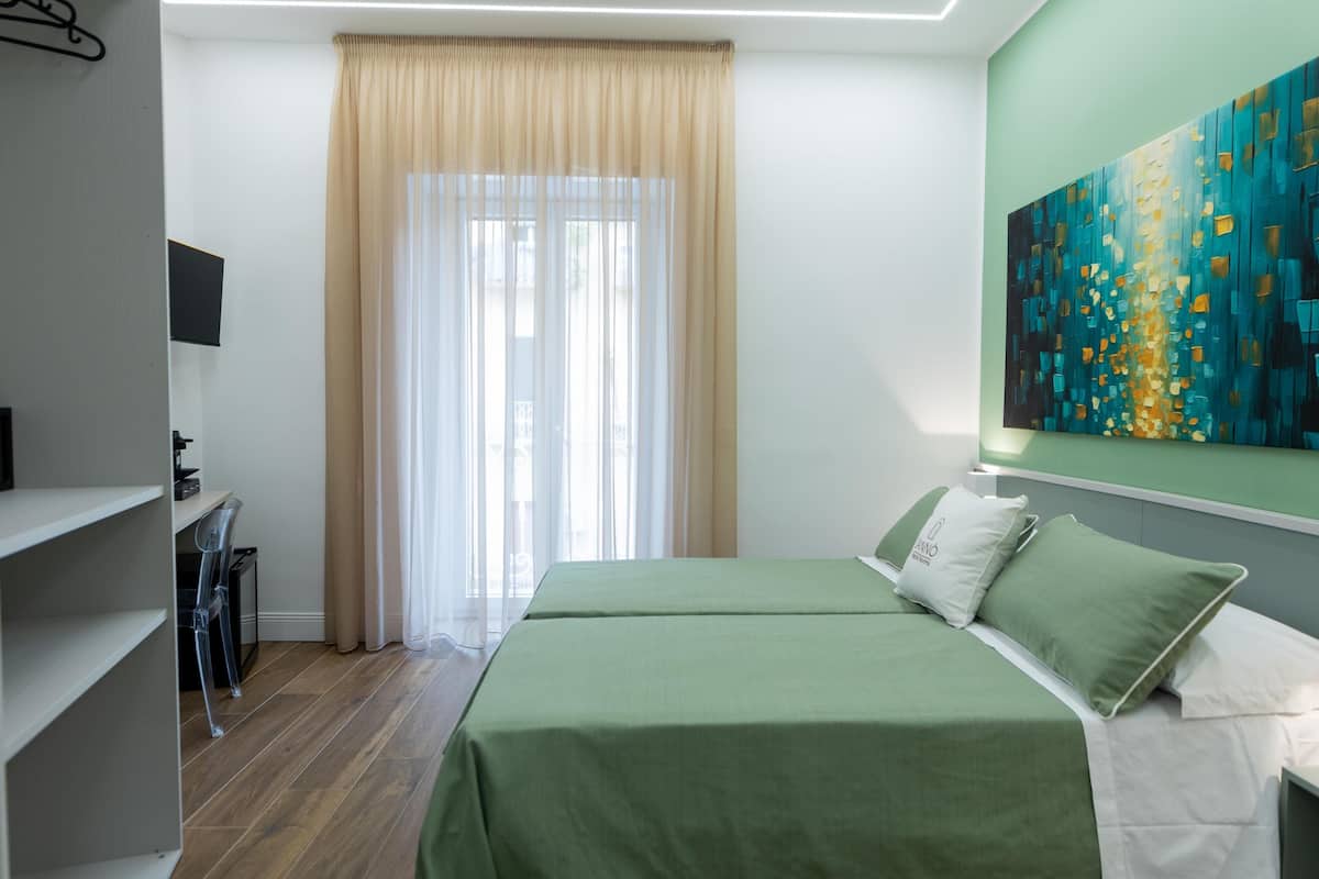 A hotel room with a bed, a desk, a chair, a TV, and a painting on the wall.
