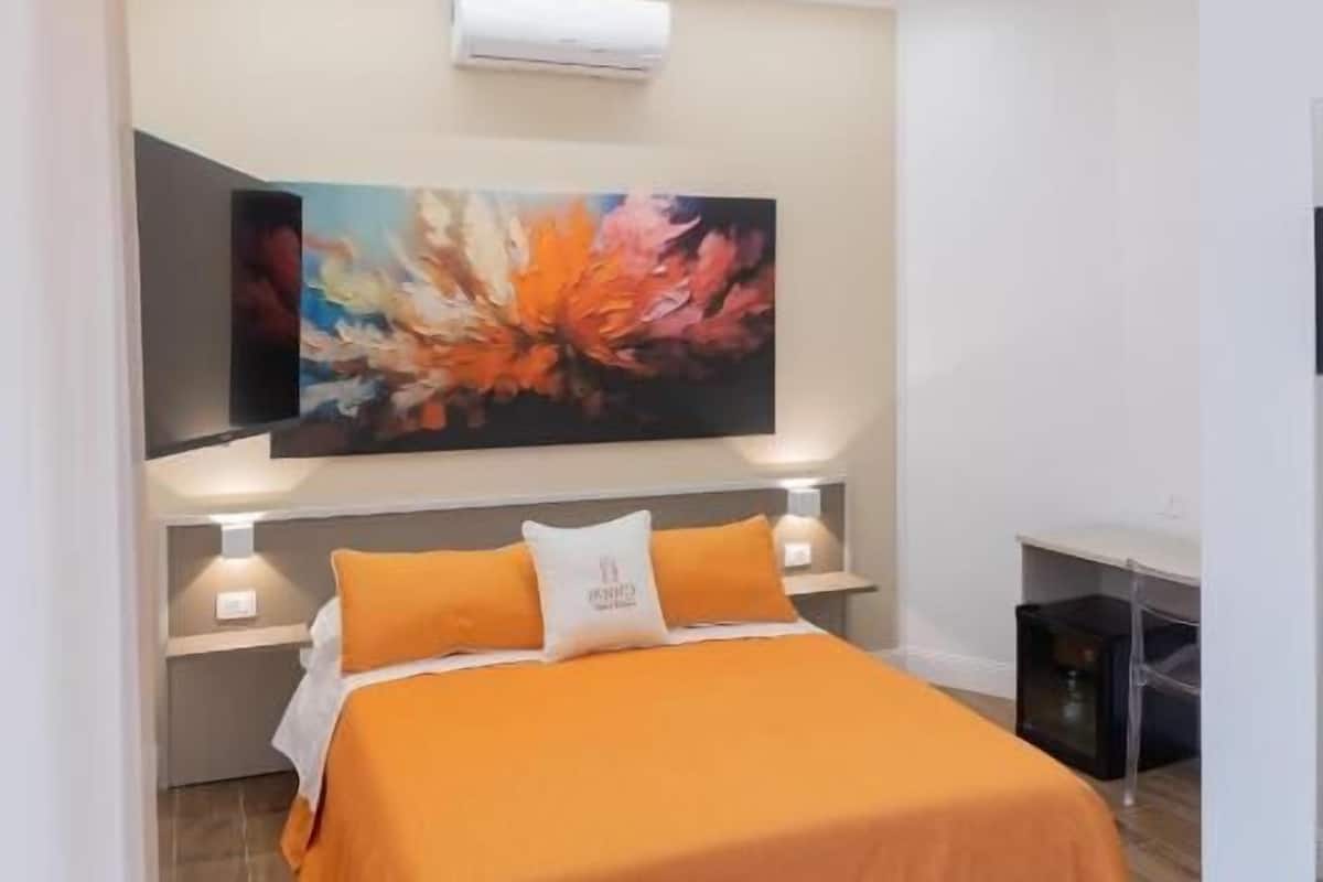 A modern bedroom with a bed, a painting, and an air conditioning unit.