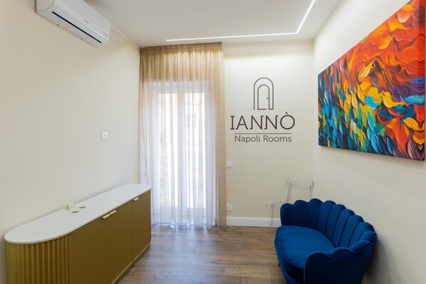 A reception area with a counter, a blue sofa, a colorful painting, and a sign for 'IANNÒ Napoli Rooms.' - Iannò Napoli Rooms (Naples)