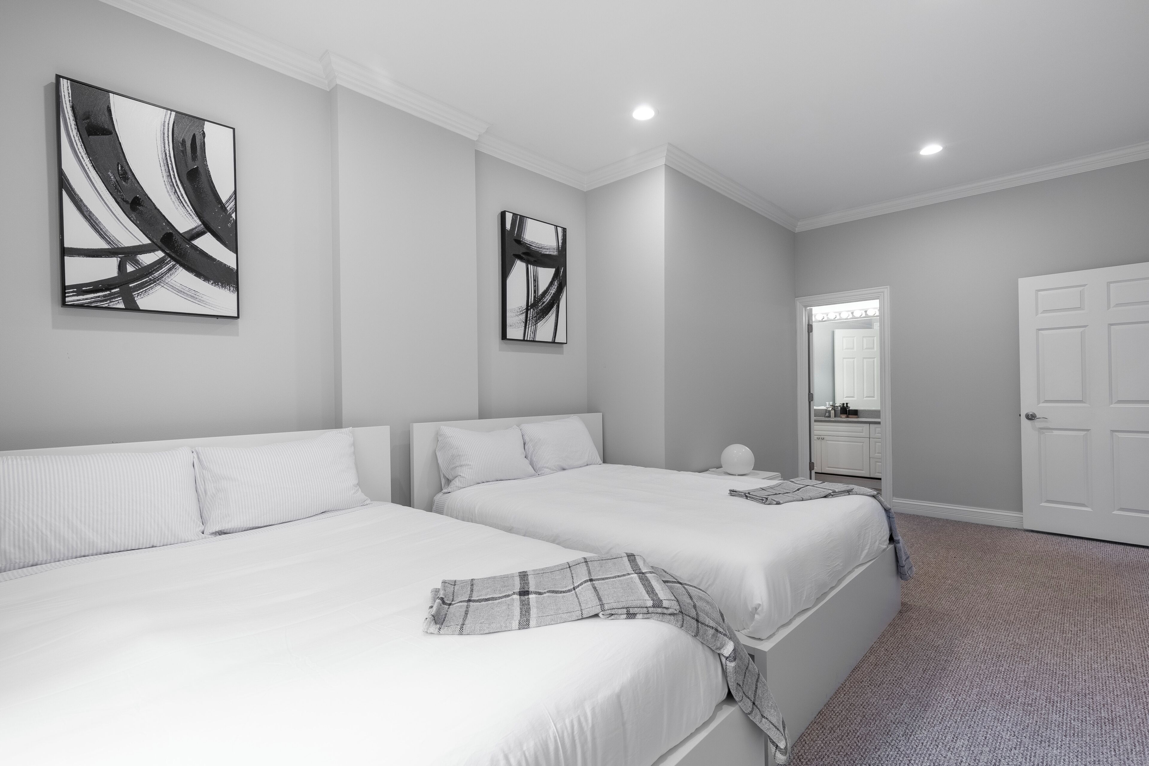 A hotel room with two beds, a large abstract painting, a mirror, and a door.