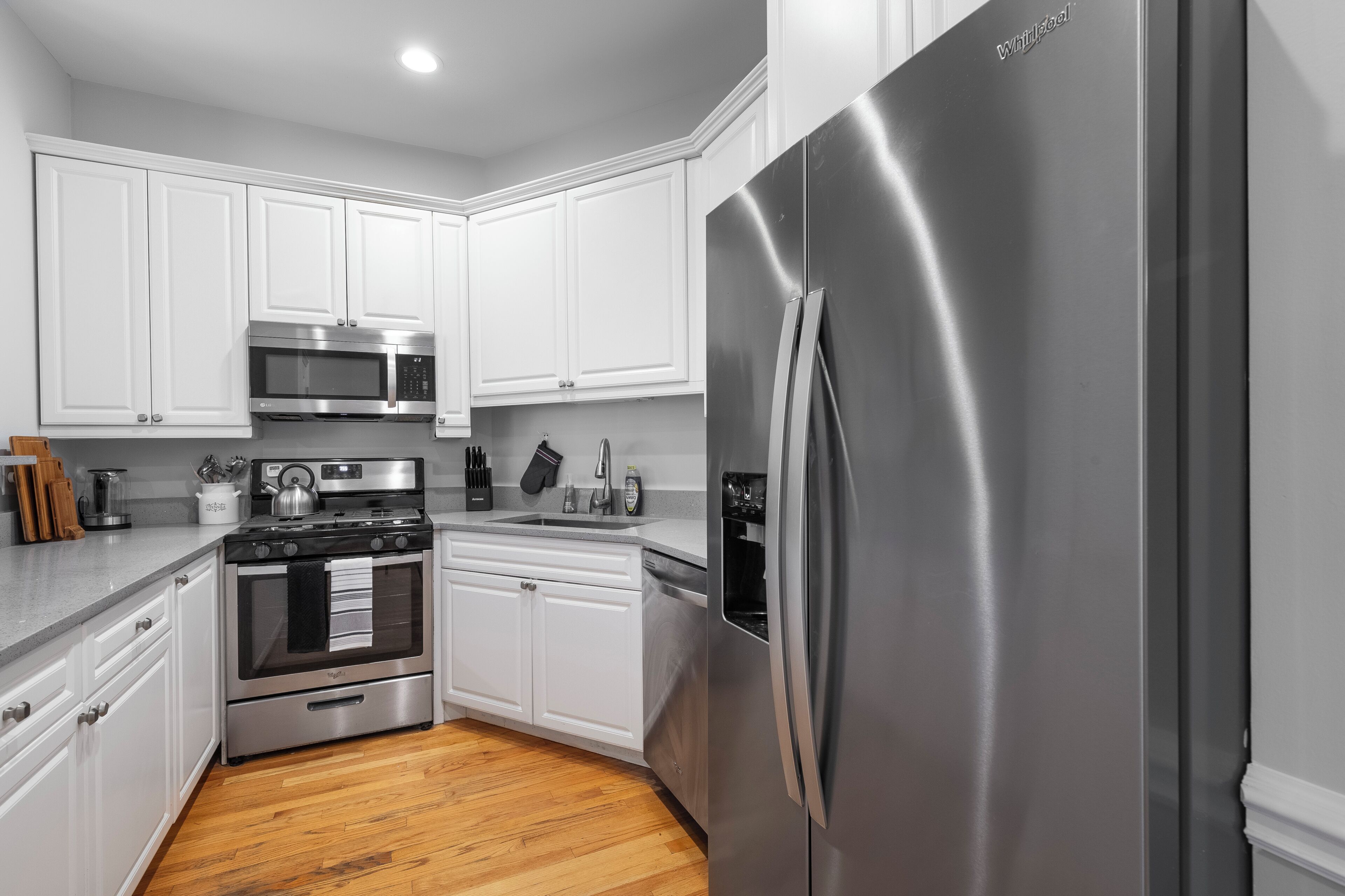 A kitchen with white cabinets, stainless steel appliances, and a wooden floor.