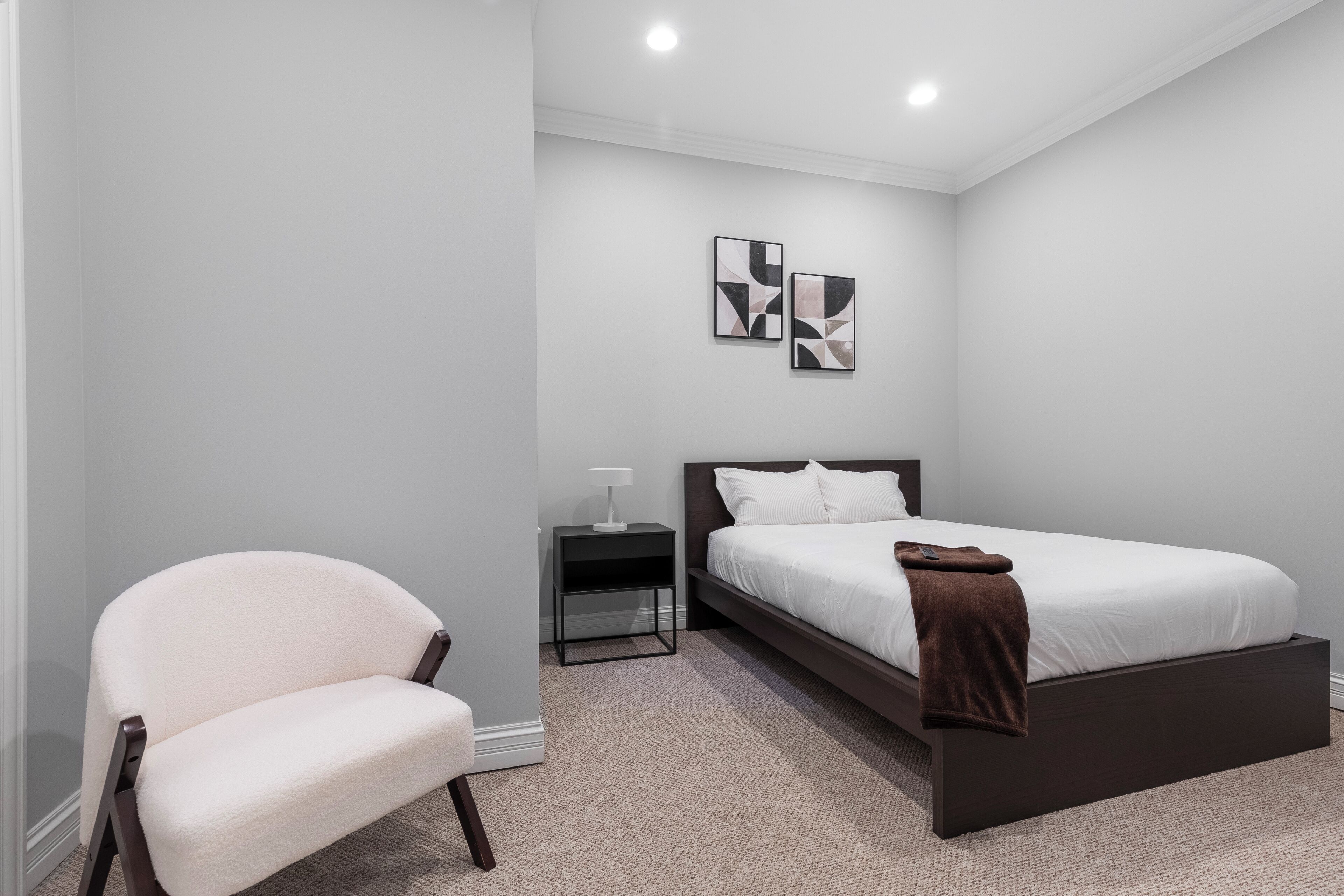 Une chambre à coucher comprenant un lit, une chaise, une table de chevet et deux œuvres d’art mural.