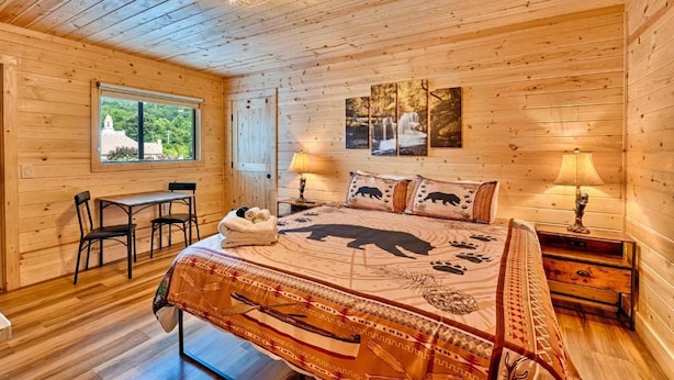 A wooden cabin bedroom with a bed, a desk, and a window. - Retreat on the Lake (Hiawassee)