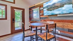 A dining area with a round table and chairs, a large wall-mounted TV, and a door leading outside. - Retreat on the Lake (Hiawassee)