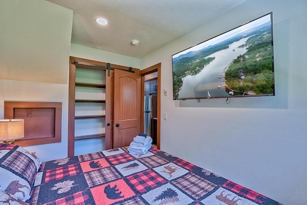 A bedroom with a bed, a TV mounted on the wall, a door, and a window.
