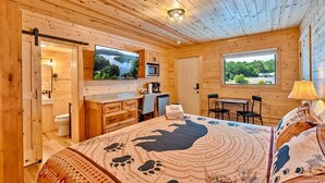 A wooden cabin bedroom with a bed, a desk, a TV, and a window with a view of the outdoors. - Retreat on the Lake (Hiawassee)