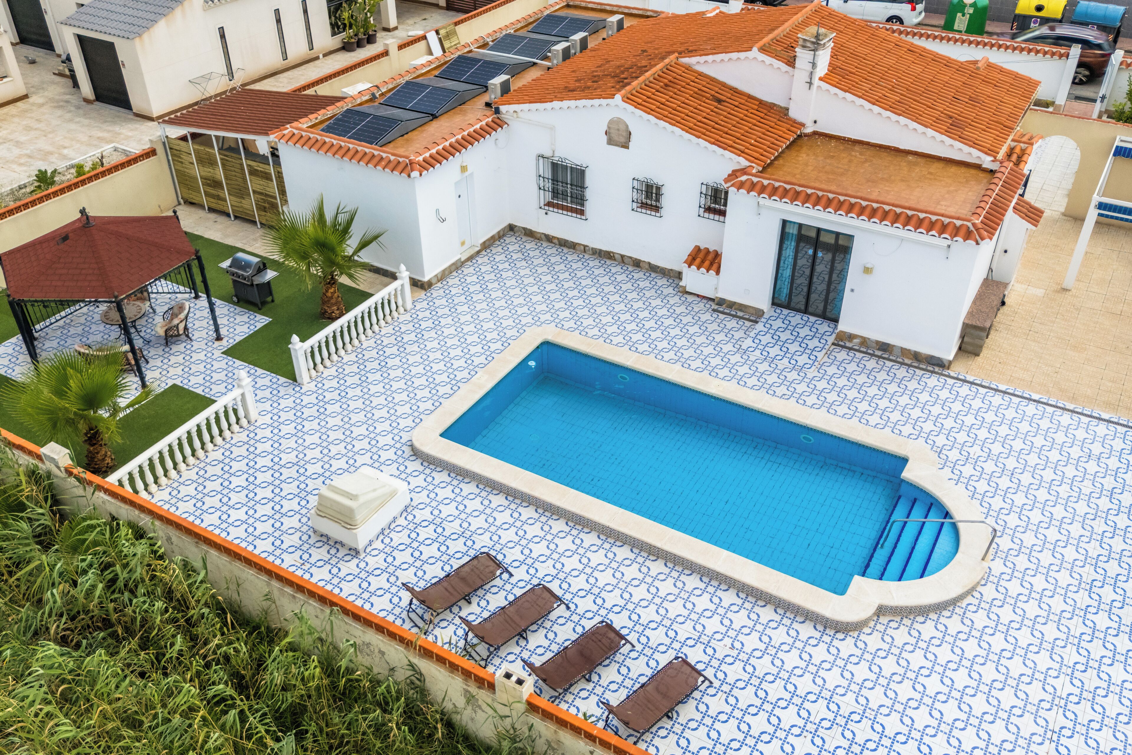 A swimming pool with a tiled deck, lounge chairs, and a covered seating area.