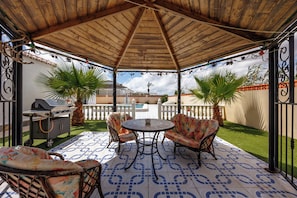 An outdoor patio with a wooden roof, a grill, two chairs, a table, and a patterned floor. - Villa Mariposa Azul with a private pool, terrace, and views of the Salt Lake (Torrevieja)