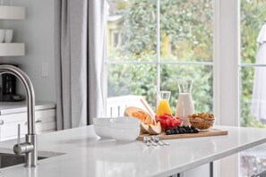 A kitchen counter with breakfast items, a window with a view of greenery, and a modern faucet. - Walk Everywhere! 16BR Retreat, 4 Pools, Sleeps 32+ (Folly Beach)