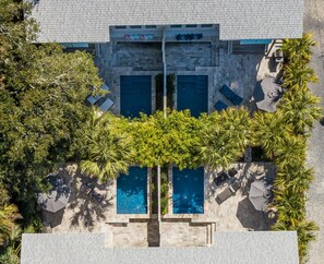 Ein Luftbild eines Hotels mit einem zentral gelegenen Schwimmbad, umgeben von Palmen und Liegestühlen.