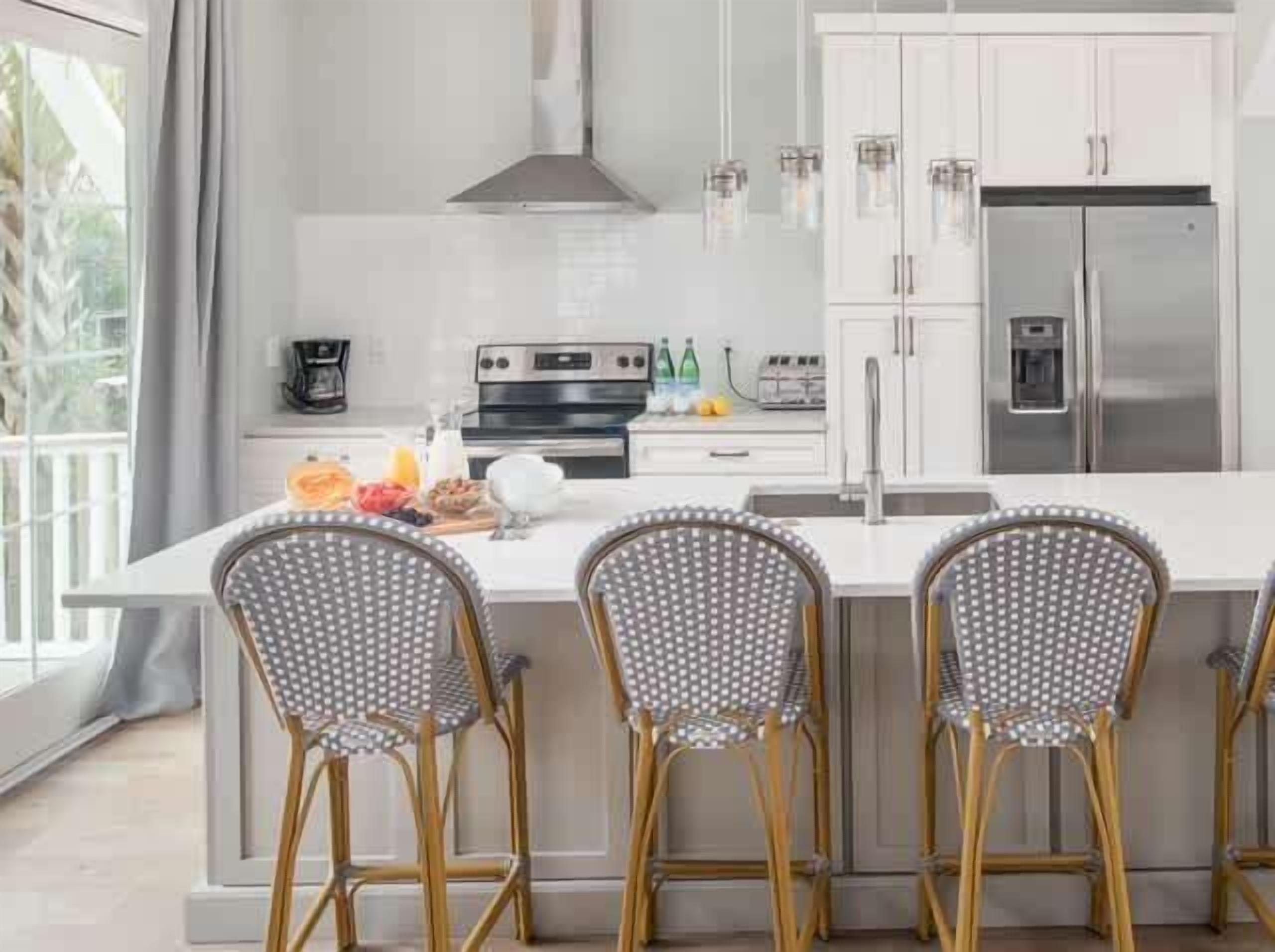 A modern kitchen with white cabinets, a stainless steel refrigerator, and a breakfast bar with four chairs.