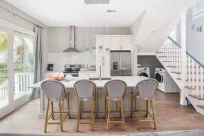 A modern kitchen with a central island, bar stools, a built-in oven, and a washing machine. - 4BR Villa with Heated Pool - Walk to The Beach & Shops (Folly Beach)