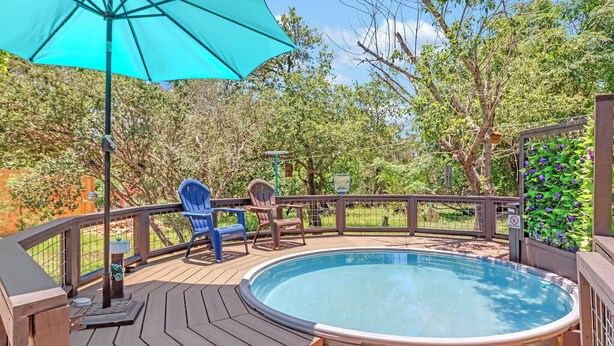 A hot tub on a wooden deck with chairs and a table, surrounded by trees and a fence. - Little Flower House | Heated Cowboy Pool, Fire Pit & Minutes to the Square (Wimberley)