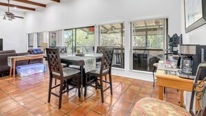 A dining area with a table, chairs, a coffee machine, and large windows. - Little Flower House | Heated Cowboy Pool, Fire Pit & Minutes to the Square (Wimberley)