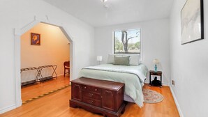A bedroom with a bed, dresser, window, and a small table with a lamp. - Little Flower House | Heated Cowboy Pool, Fire Pit & Minutes to the Square (Wimberley)