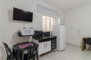 Una cuina compacta amb televisió de pantalla plana, microones, nevera, rentapelats i zona de menjador amb taula i cadire.