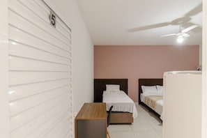 Quarto com duas camas, ventilador de teto, uma mesinha e geladeira.