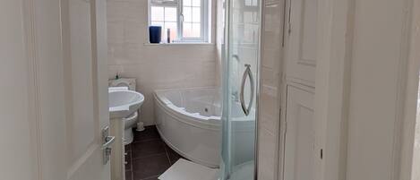 A bathroom with a bathtub, a glass-enclosed shower, a sink, and a window.