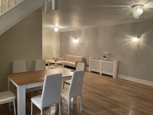 Een moderne woonkamer met een houten eettafel, witte stoelen, een beige bank en een witte console.