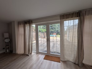 Ein Zimmer mit einer großen Schiebeglastür, die zu einem Außenbereich führt, Holzboden und einem kleinen Teppich.