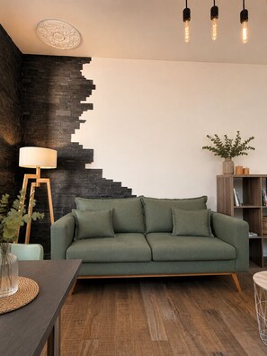 Een moderne woonkamer met een groene bank, een houten salontafel, een lamp en een boekenkast.