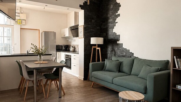 Una cocina moderna con zona de comedor, un sofá verde y un llamativo elemento decorativo en la pared negra.