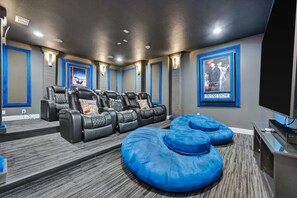 Una sala de cine en casa con varios sillones reclinables, una pantalla grande y carteles en las paredes.