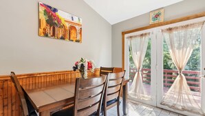 Un comedor con mesa y sillas de madera, un cuadro en la pared y vistas a través de puertas de cristal.