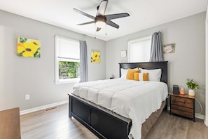 A bedroom with a bed, a ceiling fan, a nightstand, and artwork on the walls. - Lusby 5BD Family Home With Private Beach Access (Lusby)
