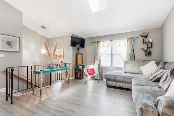 A living room with a sofa, a table, a TV, and a staircase. - Lusby 5BD Family Home With Private Beach Access (Lusby)