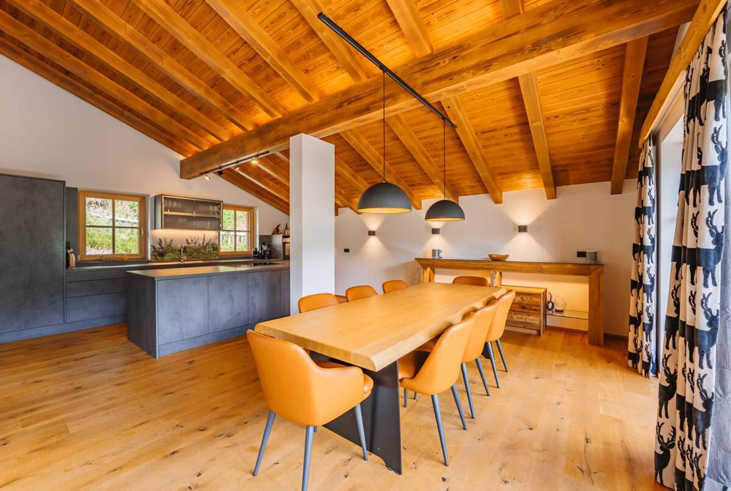 A modern kitchen with a wooden ceiling, a dining area with a long table and chairs, and a kitchen island.