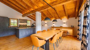 A modern kitchen with a wooden ceiling, a dining area with a long table and chairs, and a kitchen island.