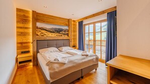 Ein Schlafzimmer mit Bett, Holzwänden, einem Fenster mit Vorhängen und Blick auf eine Landschaft.