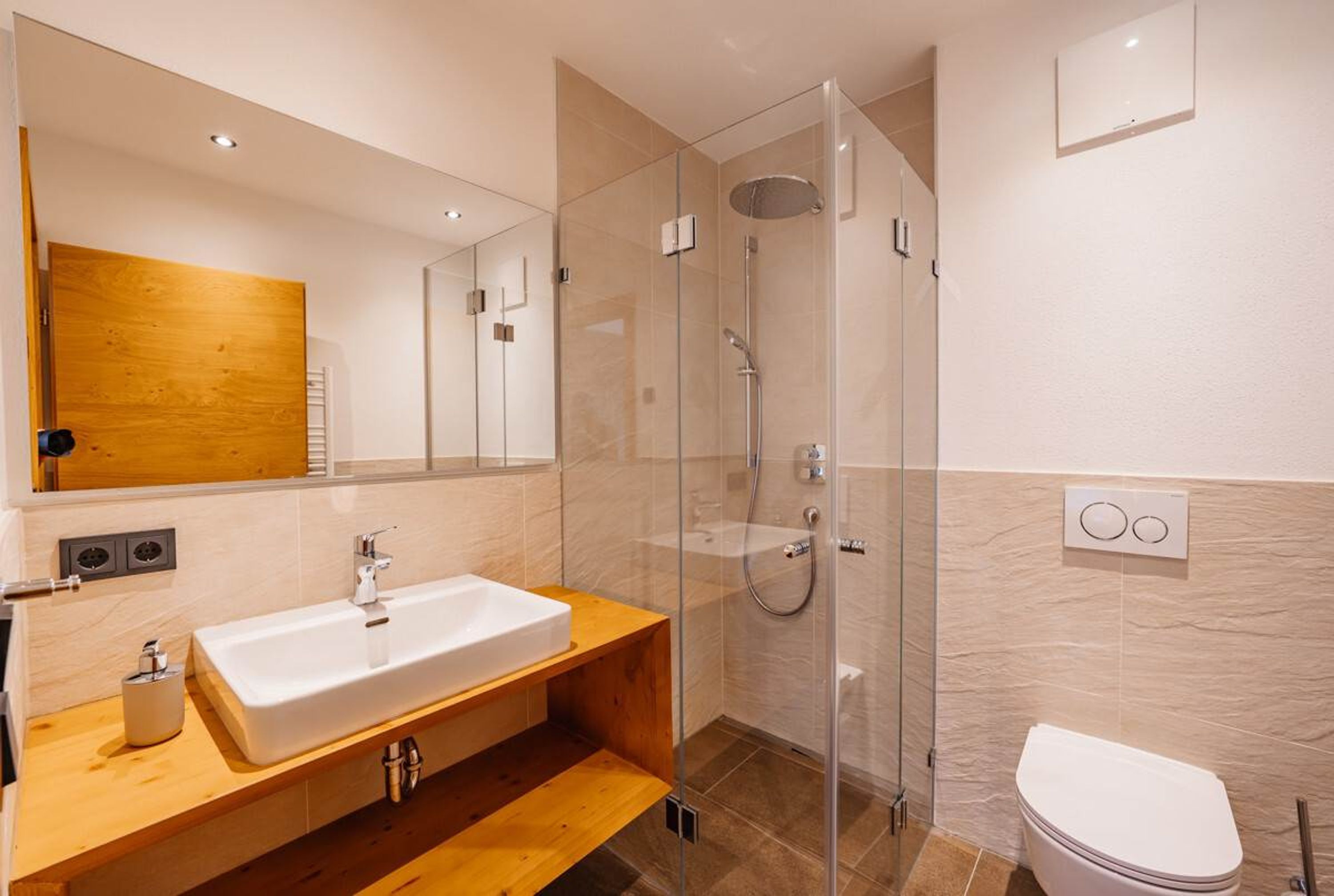 A modern bathroom with a glass-enclosed shower, a wooden vanity, and a white toilet.