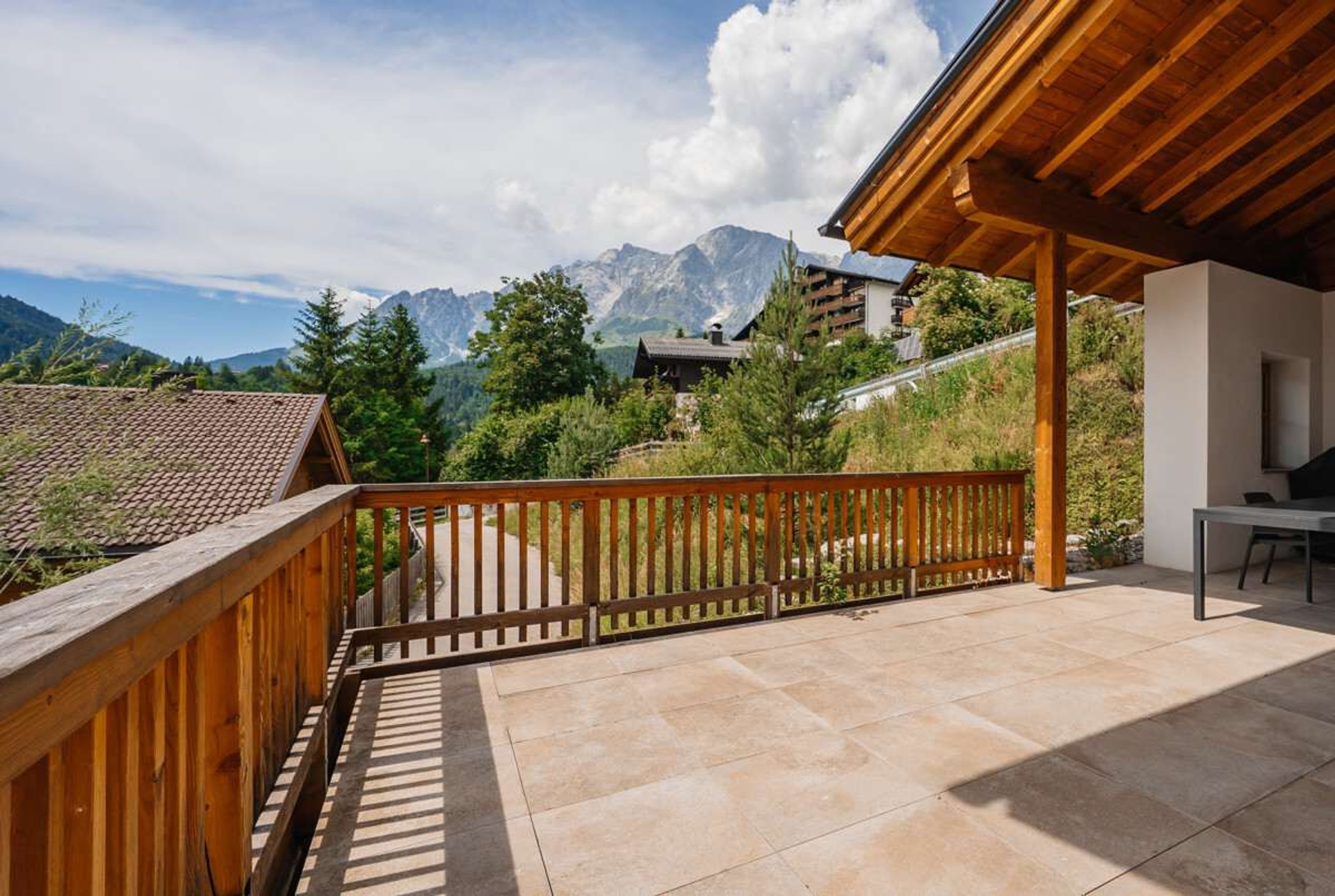 Een houten balkon met uitzicht op bergen, een overdekt terras met een tafel, en een gebouw met een pannendak.