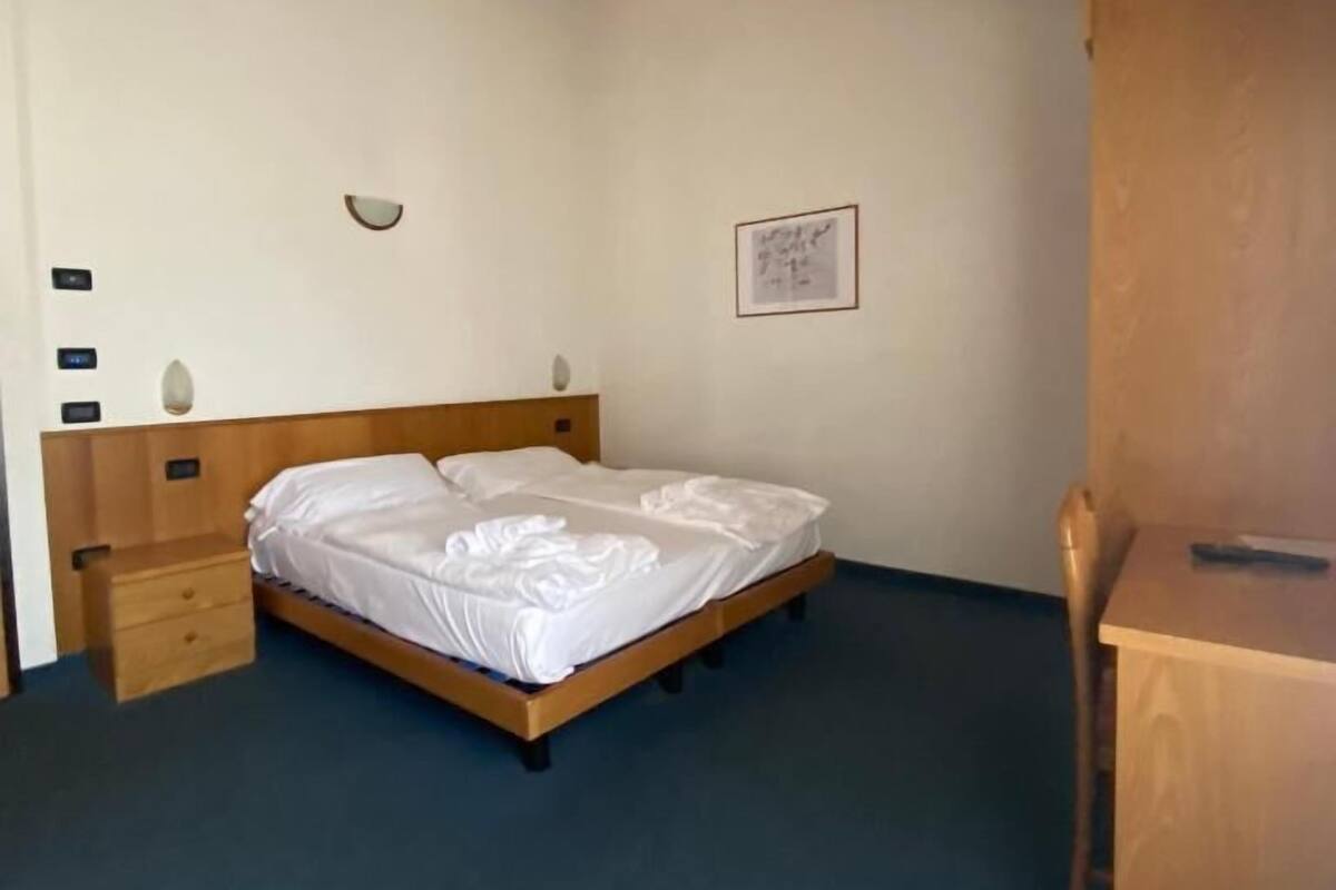 A bedroom with a wooden bed, a bedside table, a chair, and a desk.