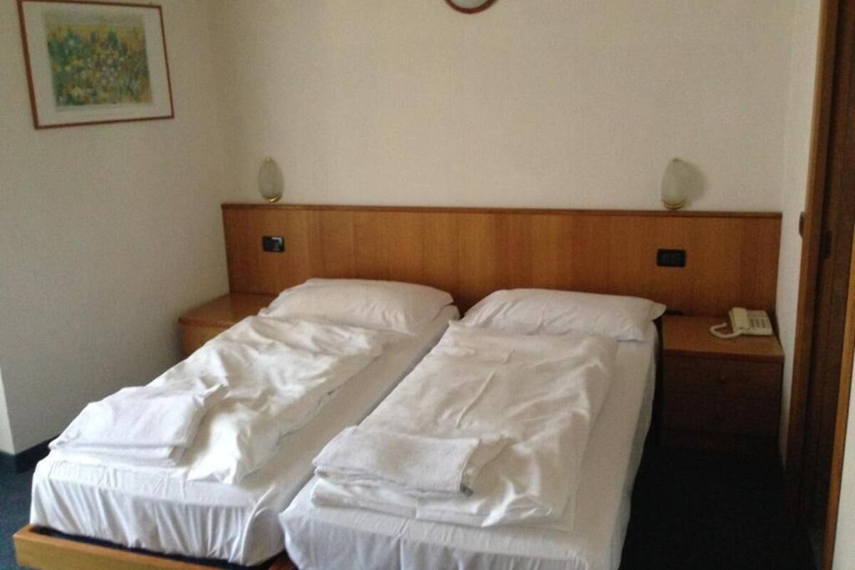A double bed with white linens, a wooden headboard, bedside lamps, a telephone, and a painting on the wall.