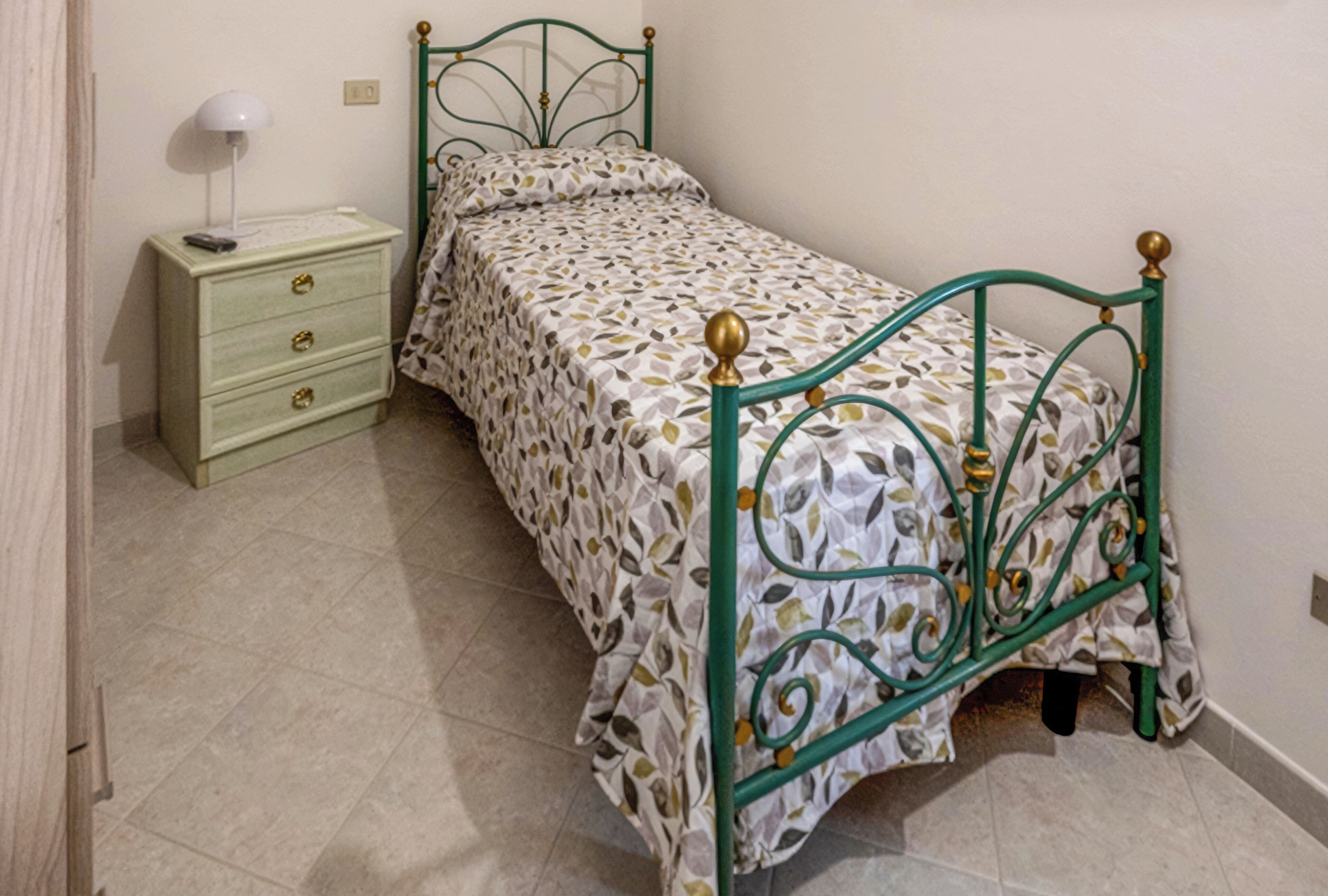 Un lit simple avec une couvre-lit à motifs, une table de chevet avec une lampe et une commode.