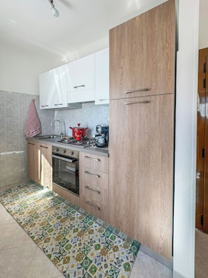 A modern kitchen with white cabinets, a wooden accent wall, a patterned floor, and a red kettle. - Casa Marinella (Porchia)