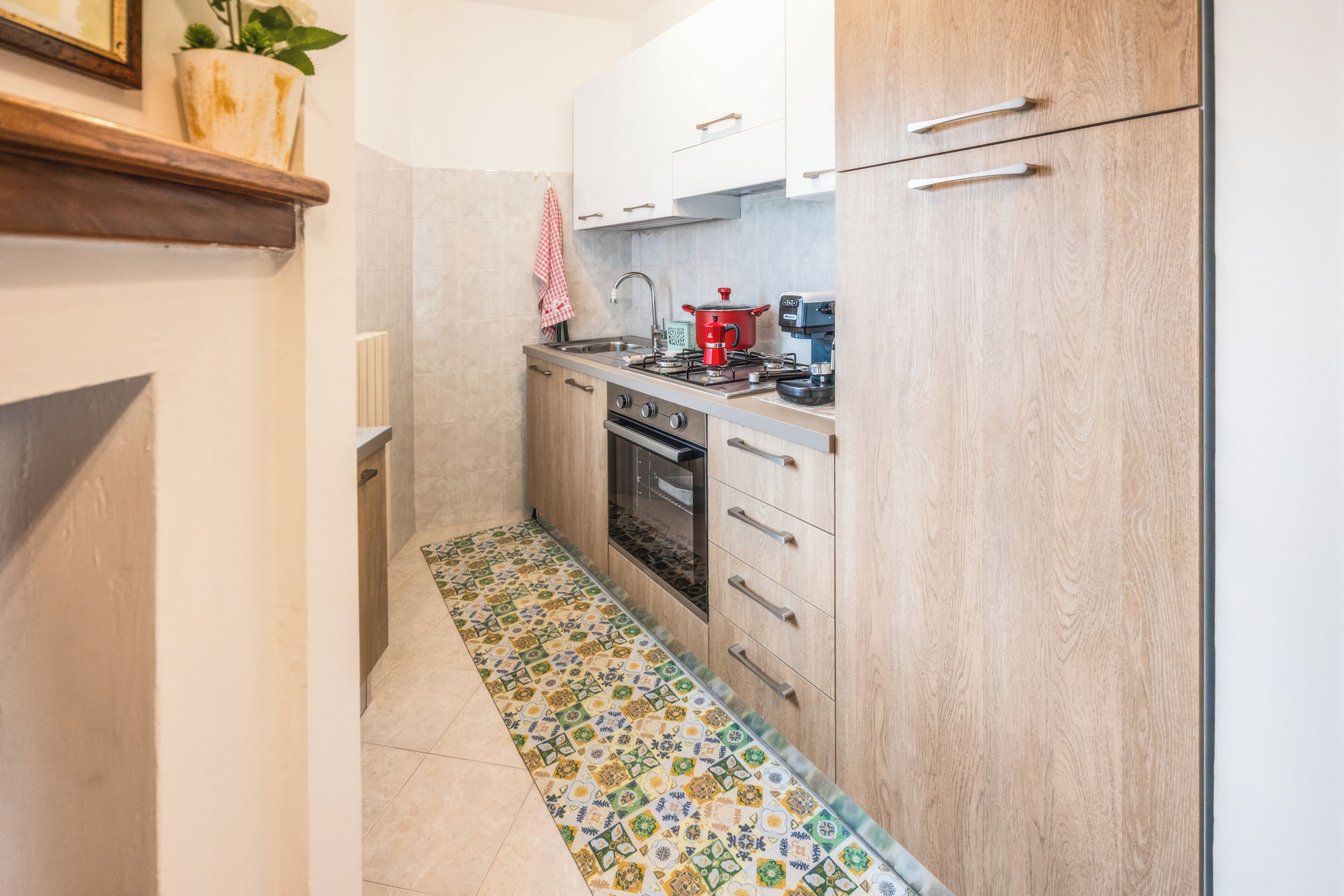 A compact kitchen with a tiled floor, a stove, a sink, and wooden cabinets.