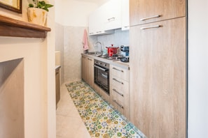 A compact kitchen with a tiled floor, a stove, a sink, and wooden cabinets. - Casa Marinella (Porchia)