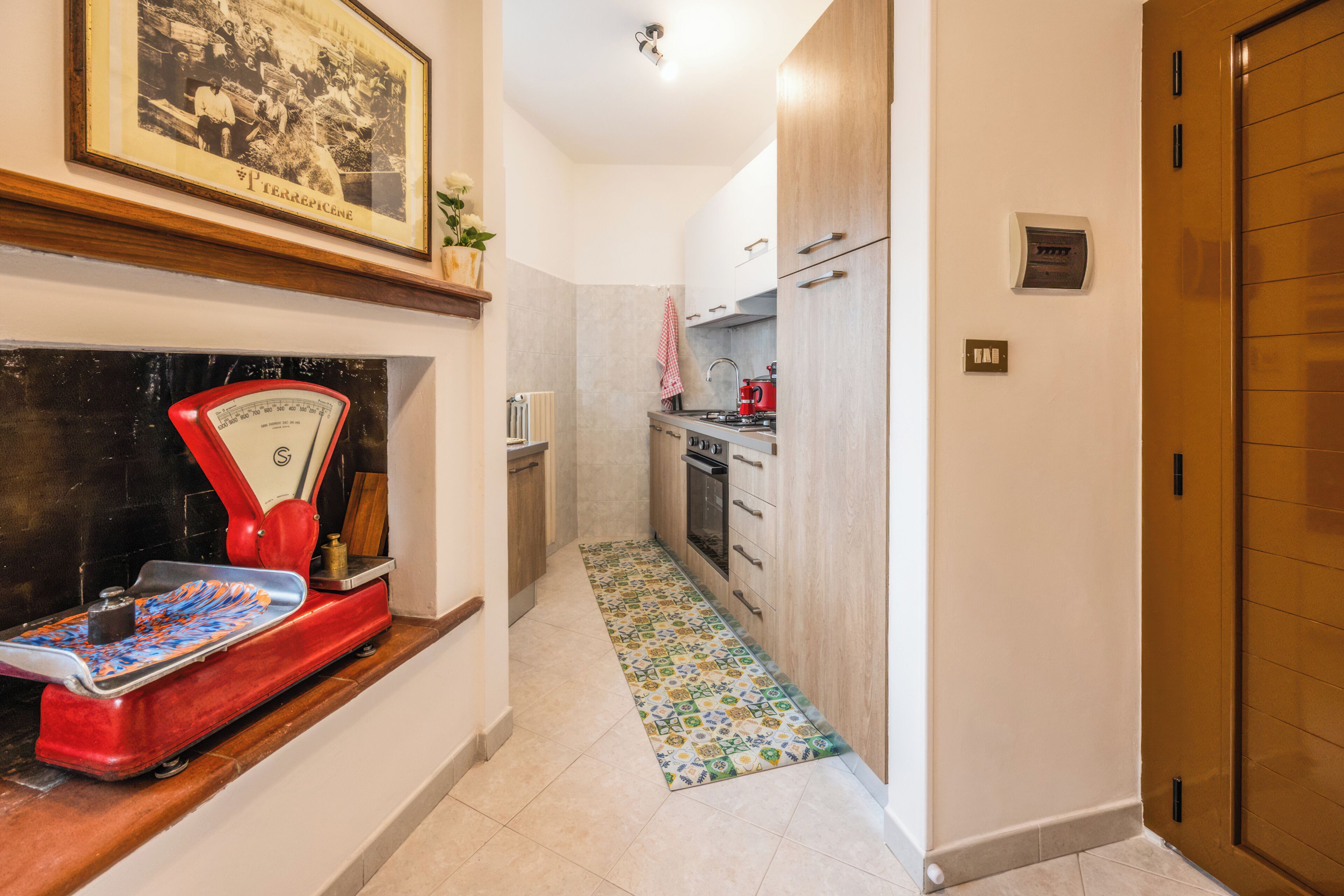 A narrow hallway with a kitchen area, a scale, a radiator, and a patterned rug.