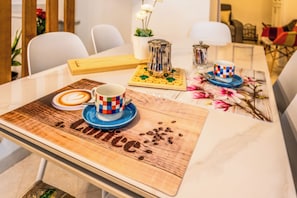 A dining table with a coffee cup, a coffee pot, and a wooden placemat with the word 'Coffee' on it.