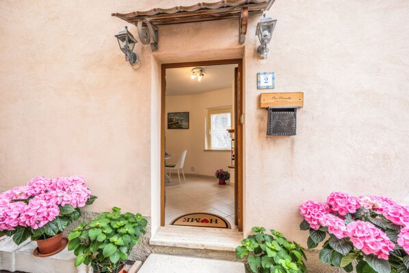 Une porte d’entrée avec un paillasson sur lequel est écrit « MAISON », une enseigne en bois et une petite boîte aux lettres.