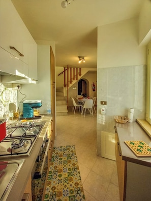 A kitchen with a gas stove, a coffee machine, and a dining area with a table and chairs. - Casa Marinella (Porchia)